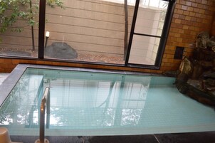 An indoor swimming pool with clear water, a tiled floor, and a stone wall with a rock feature.