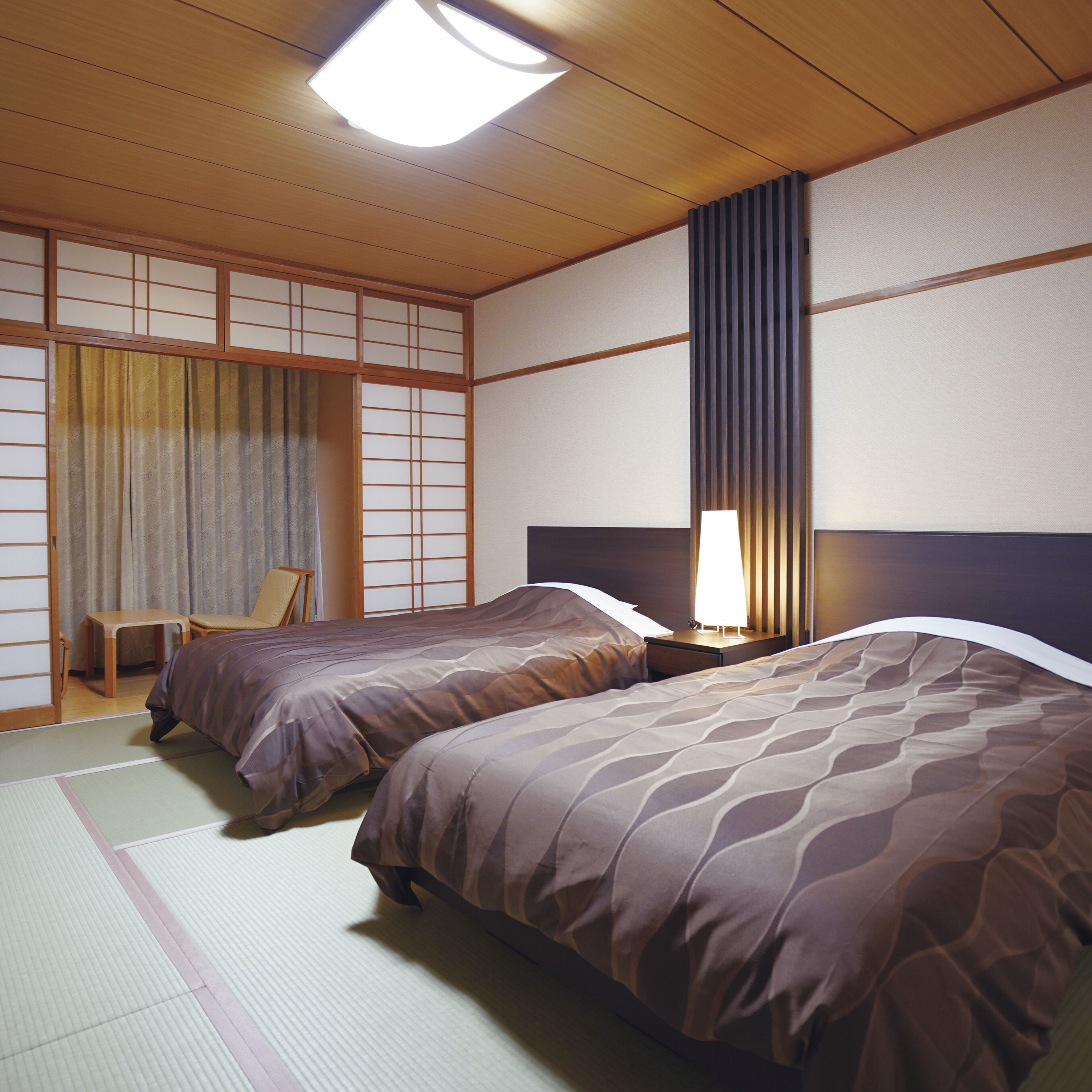 A traditional Japanese room with tatami flooring, two beds with matching bedding, a desk, and a chair.