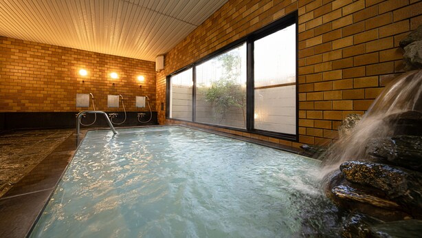 A spa area with a hot tub, a waterfall feature, and a brick wall with windows. - The Gran Resort Elegante Karuizawa (Karuizawa)