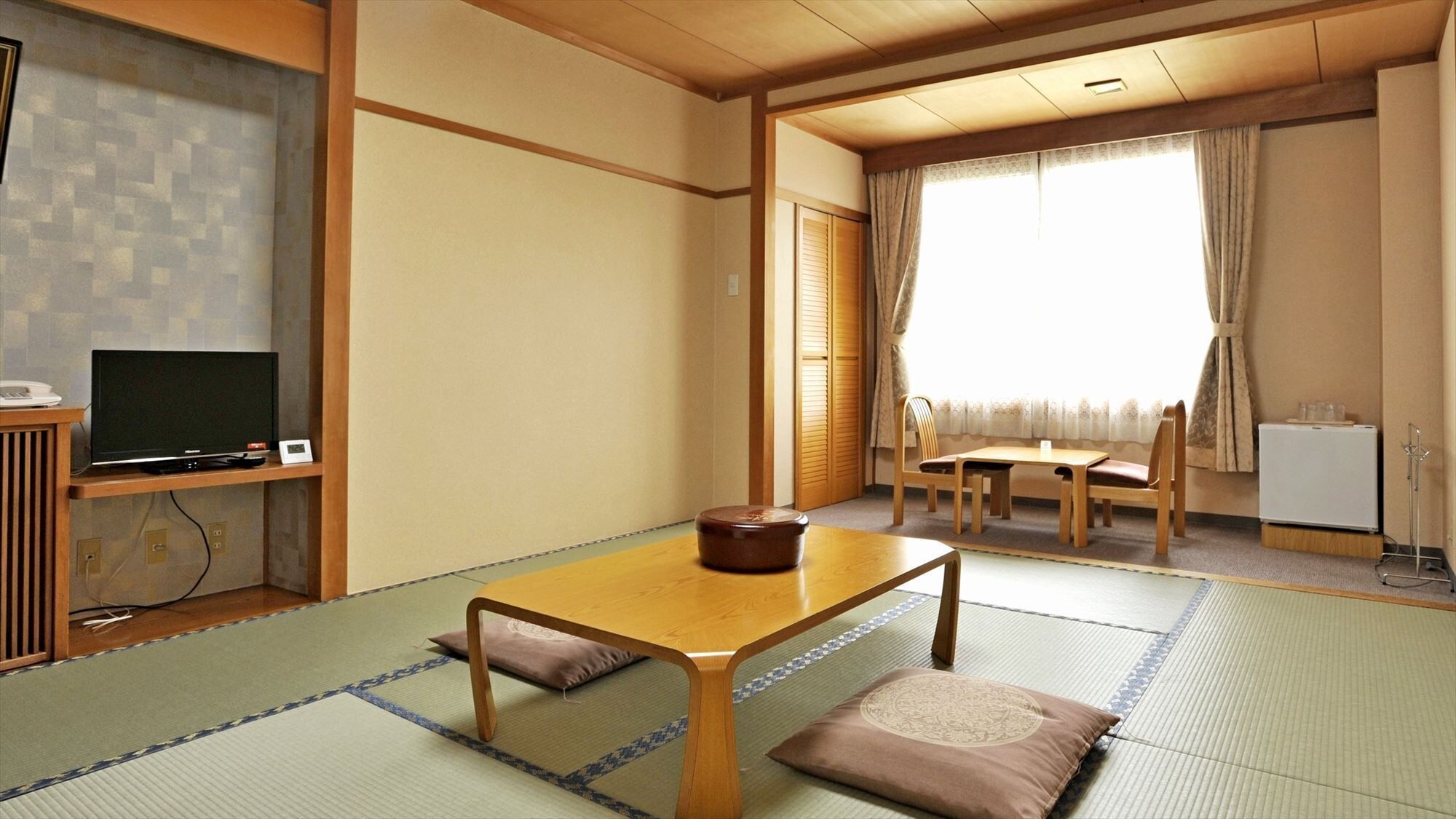Um quarto japonês tradicional com tatame, uma televisão, uma mesa com almofadas e uma porta deslizante.