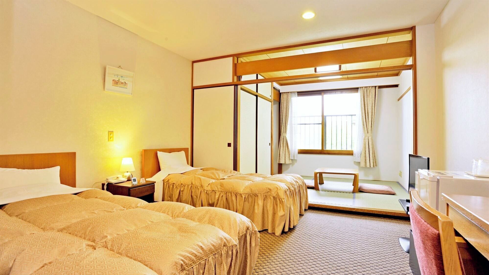 A hotel room with two beds, a desk, a chair, a TV, and a window with curtains.