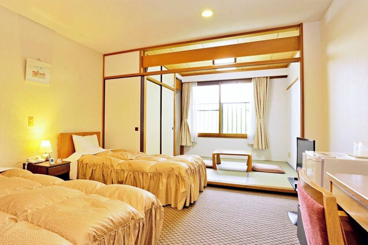 A hotel room with two beds, a desk, a chair, a TV, and a window with curtains.