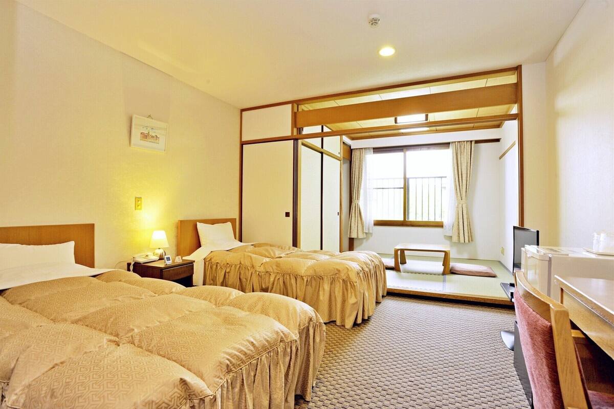 A hotel room with two beds, a desk, a chair, a mirror, and a window with curtains.