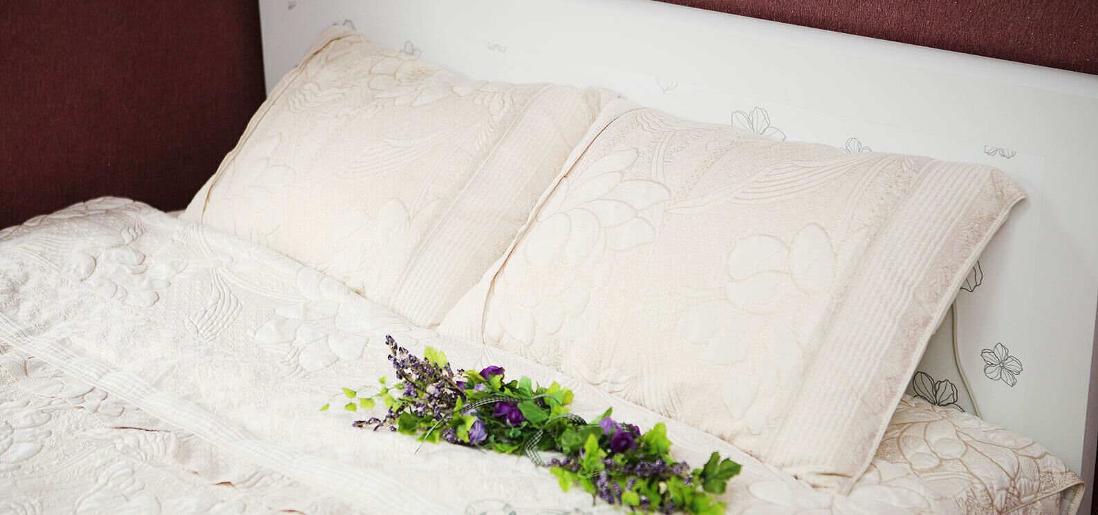 A bed with a white headboard and pillows, a floral arrangement on the bed, and a white wall with a subtle floral pattern.