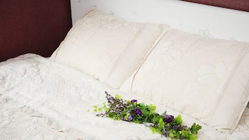A bed with a white headboard and pillows, a floral arrangement on the bed, and a white wall with a subtle floral pattern.