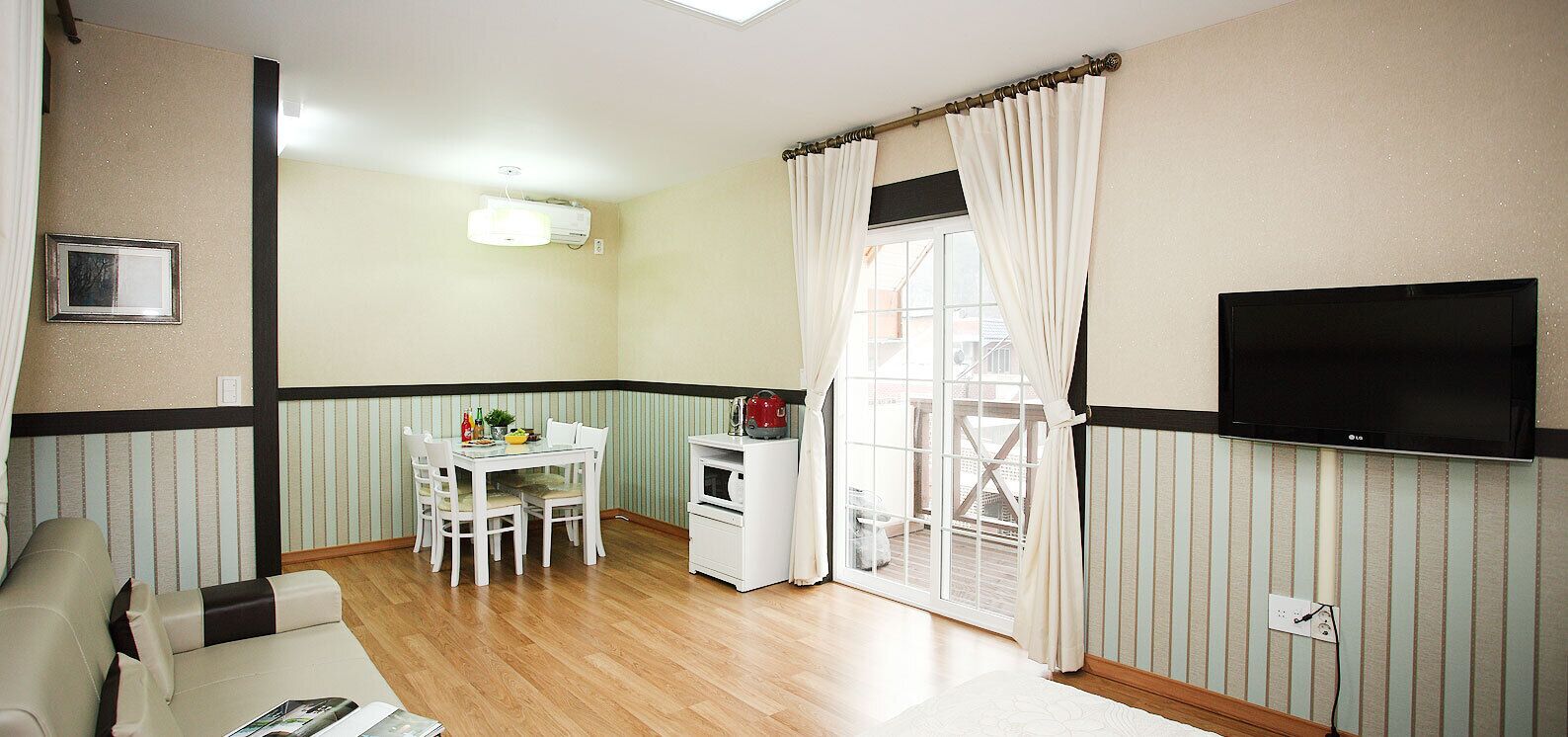 A compact living space with a dining area, a TV mounted on the wall, and a window with curtains.