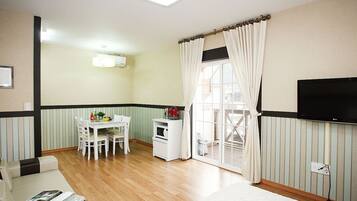 A compact living space with a dining area, a TV mounted on the wall, and a window with curtains.