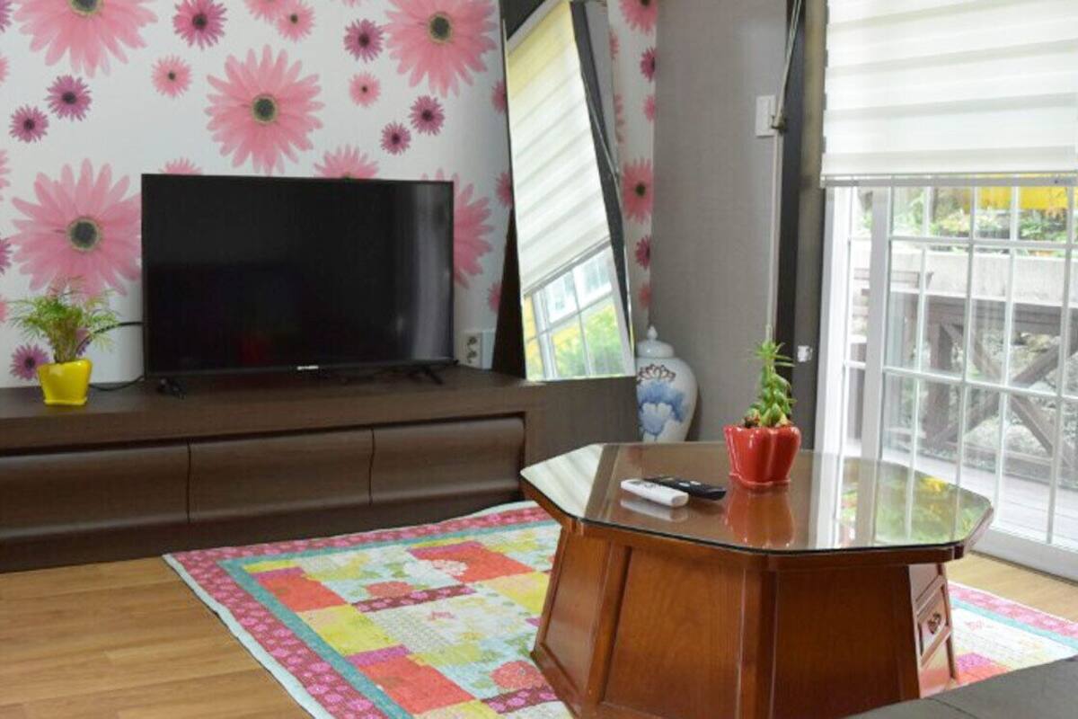 Ein Wohnzimmer mit Flachbildfernseher, Mikrowelle, Holzschrank, Glastisch und einem farbenfrohen Teppich.