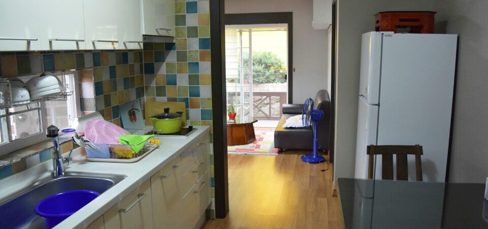 A kitchen with a sink, a stove, and a refrigerator. There is a window with a view of the outside.