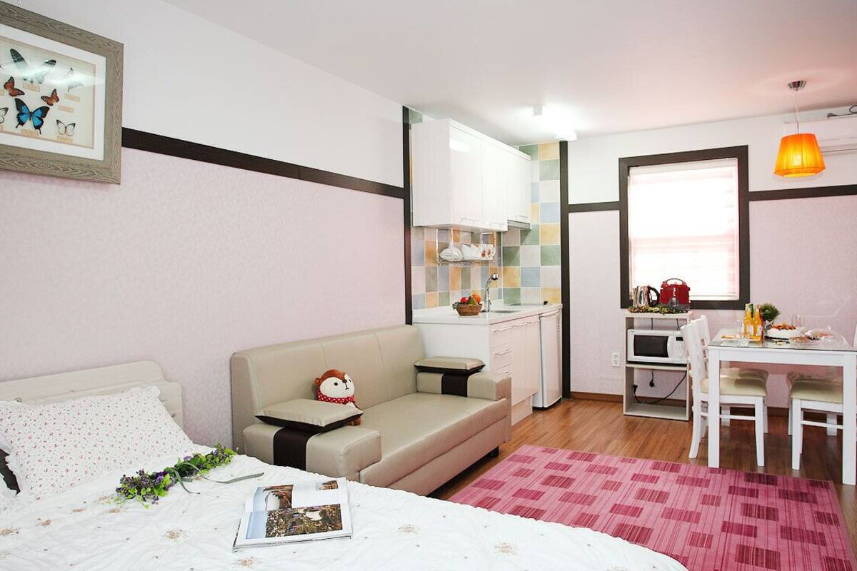 Ein gemütliches Schlafzimmer mit Bett, einer kleinen Couch, einem Esstisch mit Stühlen, einer Küchenzeile und einem Fenster mit Aussicht.