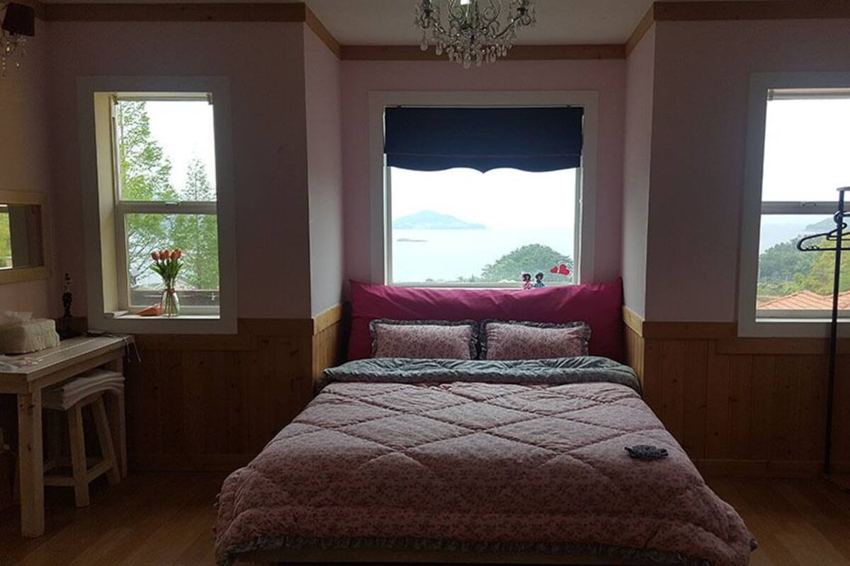 Une chambre à coucher comprenant un lit, une commode, un miroir, une fenêtre donnant sur un beau paysage et un lustre.
