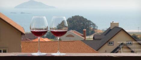 Two wine glasses on a balcony with a view of houses and a distant island.