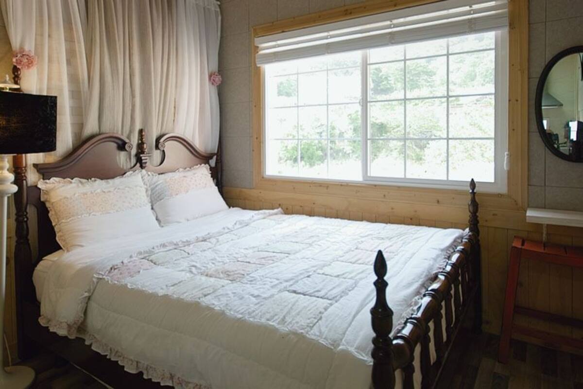 Une chambre à coucher avec un lit en bois, une table de chevet, un miroir et une fenêtre avec des rideaux.