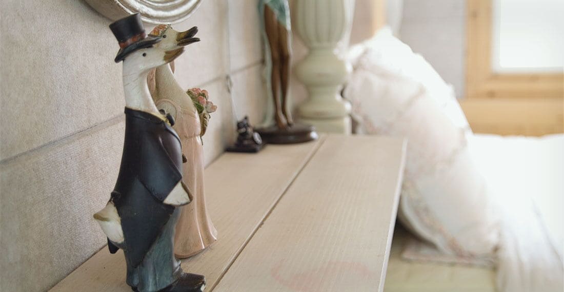 A room with a wooden floor, a white bed, and a wall-mounted shelf with decorative items.