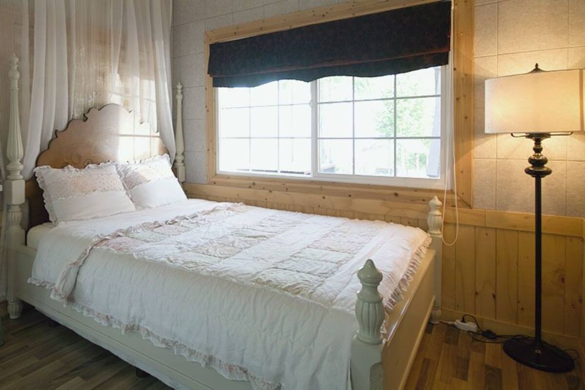 Une chambre à coucher avec un lit à baldaquin, une table de chevet, une lampe et une fenêtre donnant sur un paysage verdoyant.