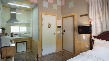 Une chambre d’hôtel compacte comprenant un coin cuisine, une salle de bain séparée et un lit avec une table de chevet.