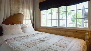 Una cama con cabecera de madera, ropa de cama blanca y ventana con vistas a la vegetación.