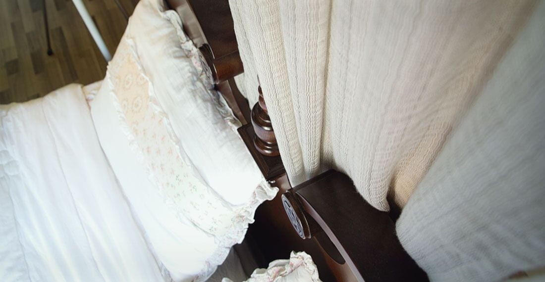 A close-up of a bed with white linens and a wooden headboard.