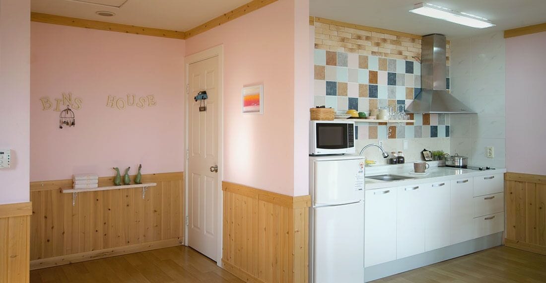 A kitchen with white cabinets, a microwave, a stove, and a sink. There is a wooden door and a shelf with decorative items.