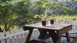 Una mesa de picnic de madera con dos tazas marrones y un jarrón de flores moradas.