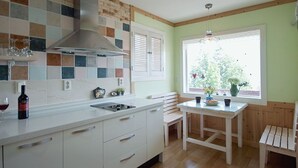 Una cocina con armarios blancos, salpicadero de azulejos, una ventana con persianas y un banco de madera.