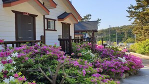 A two-story building with a porch and a garden with pink and white flowers. - Haesol Maru Pension Taean (Taean)