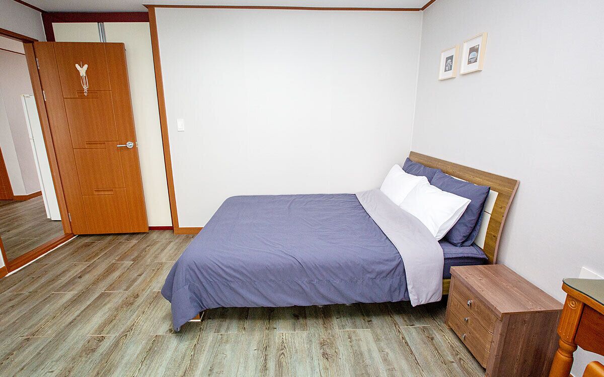 A bedroom with a bed, wooden nightstand, and a door.
