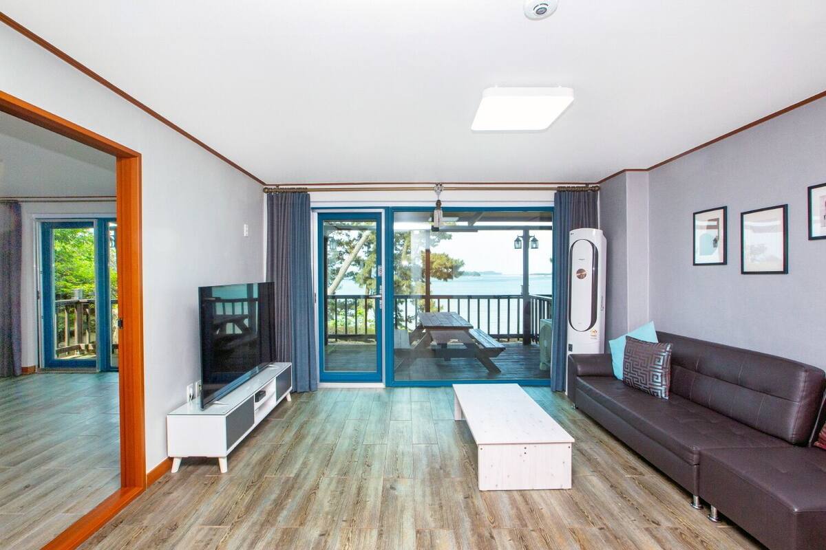 A modern living room with a TV, sofa, and a view of a balcony with a table and chairs.