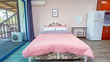 A bedroom with a bed, a small table, a refrigerator, and a window with curtains.