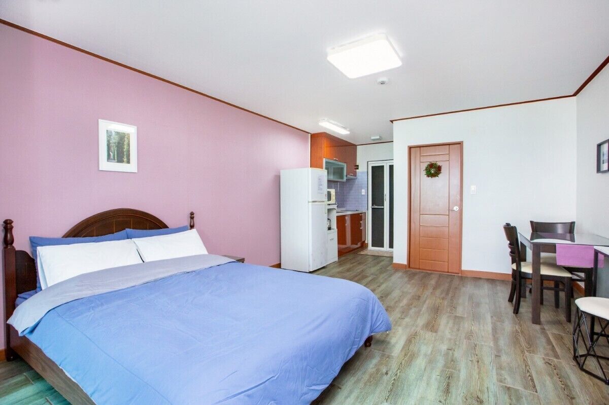 A bedroom with a bed, a desk, and a kitchenette.