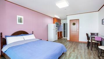 A bedroom with a bed, a desk, and a kitchenette.