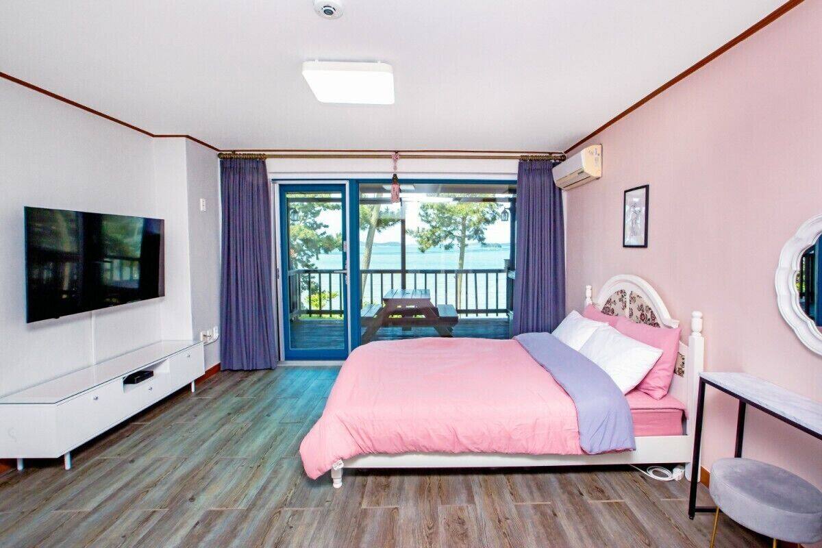 A bedroom with a bed, a TV, a desk, and a view of the outdoors.