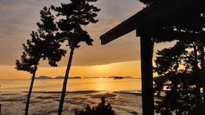 A beach view with a sunset, trees, and a structure with a roof. - Haesol Maru Pension Taean (Taean)