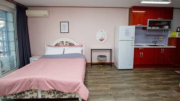Een slaapkamer met een bed, een klein nachtkastje, een spiegel, en een kitchenette met een koelkast en magnetron.