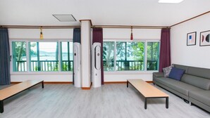 A room with two large windows, a grey sofa, a wooden bench, and two air conditioning units. - Haesol Maru Pension Taean (Taean)
