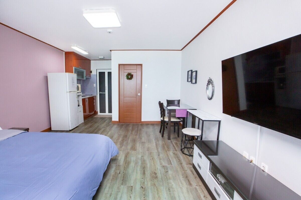 Habitación de hotel pequeña con cama, escritorio con silla, televisión y kitchenette.