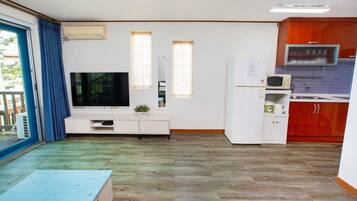 A compact living space with a kitchenette, a flat-screen TV, and a sliding glass door leading to an outdoor area.