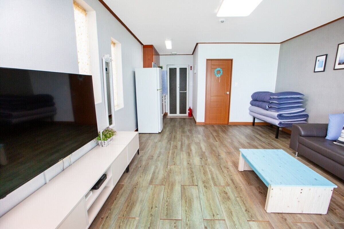 A living room with a flat-screen TV, a white cabinet, a blue bench, a gray sofa, and a wooden floor.