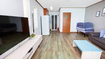 A living room with a flat-screen TV, a white cabinet, a blue bench, a gray sofa, and a wooden floor.