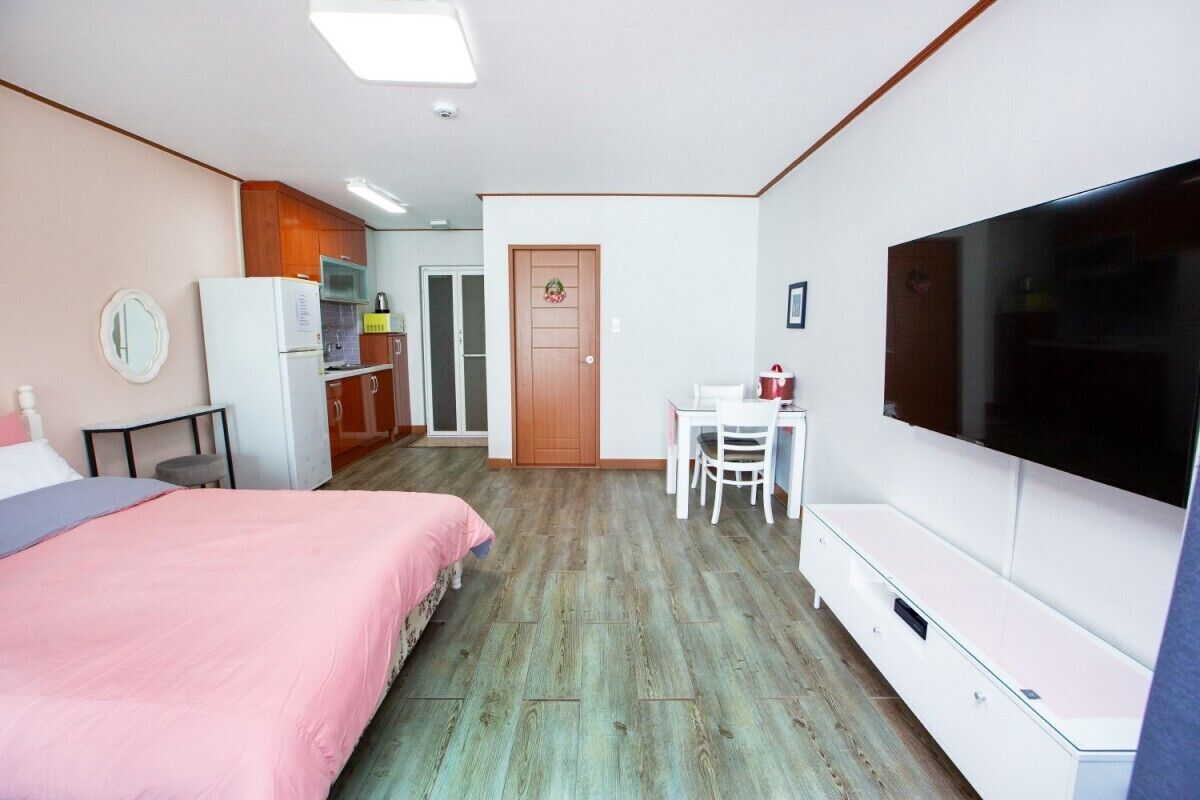Een slaapkamer met een bed, een bureau, een televisie en een kitchenette.