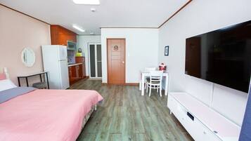 Een slaapkamer met een bed, een bureau, een televisie en een kitchenette.