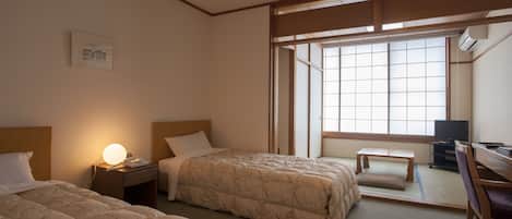A hotel room with two beds, a desk, a chair, a television, and a large window providing natural light.