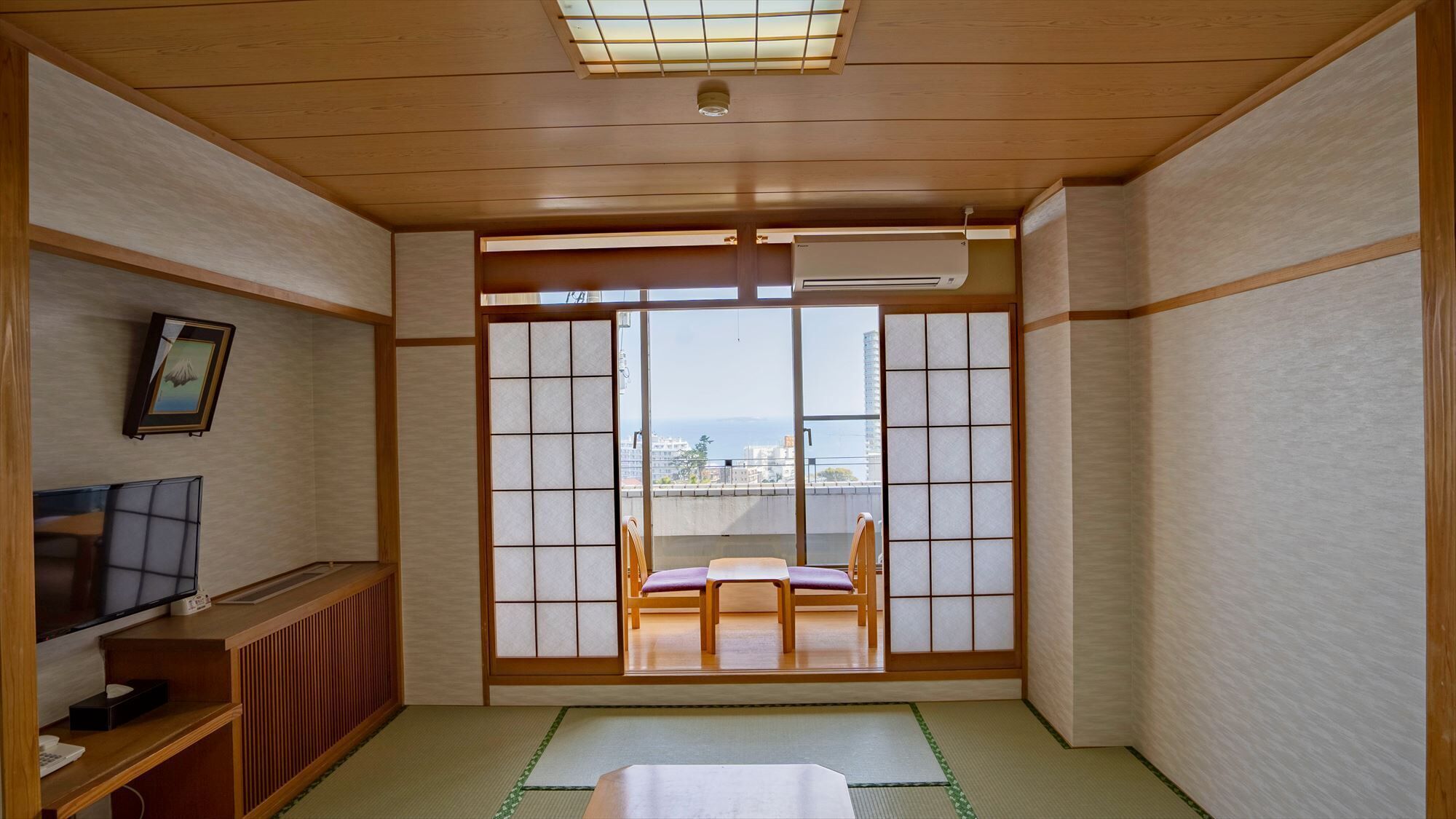 Una tradizionale stanza giapponese con pavimento in tatami, un futon, una televisione e vista sulla città attraverso delle porte scorrevoli shoji.