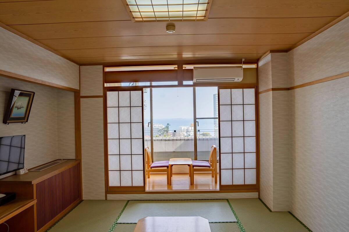 Una tradizionale stanza giapponese con pavimento in tatami, un futon, una televisione e vista sulla città attraverso delle porte scorrevoli shoji.