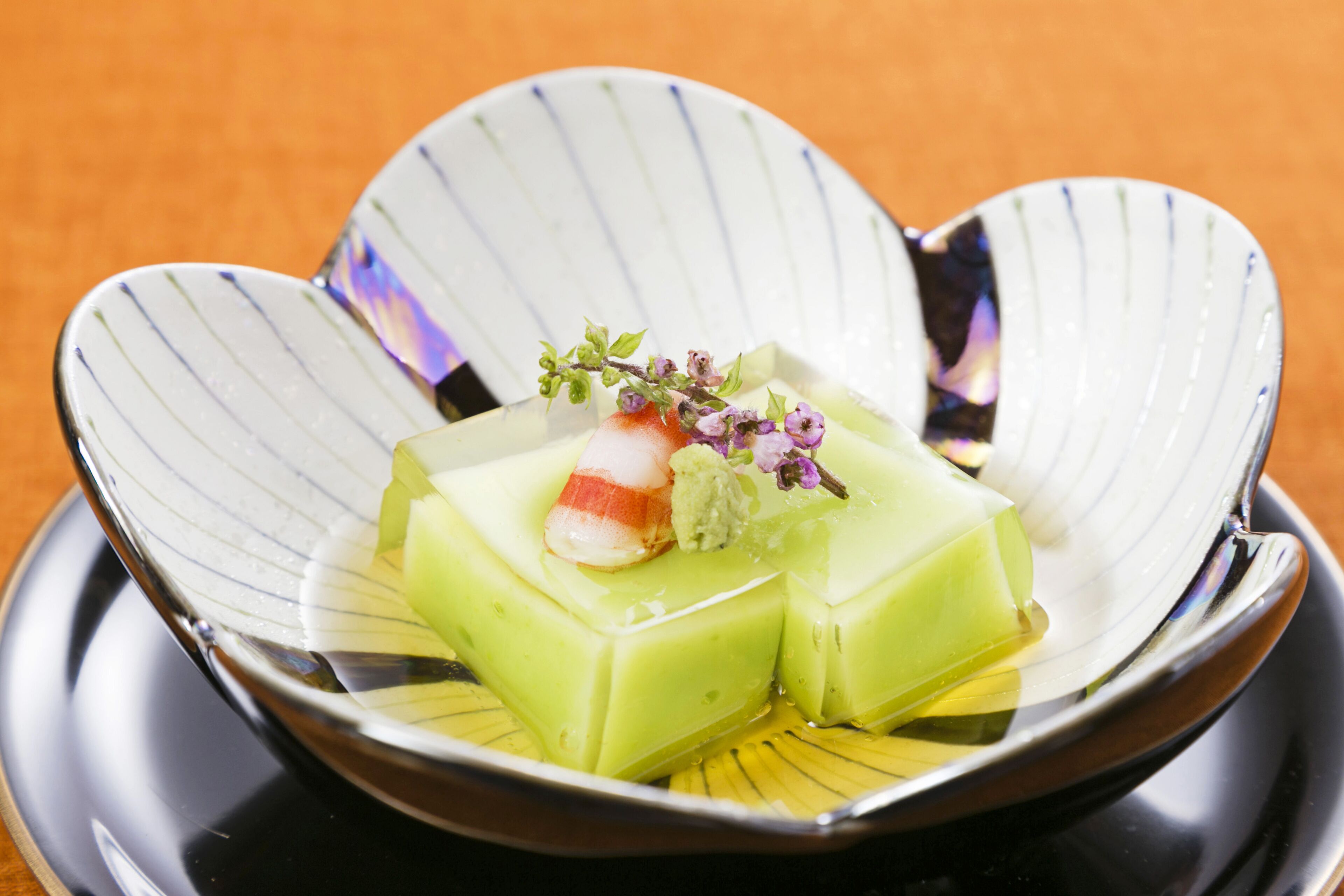 A dish with green cubes and a slice of fish on a decorative plate.