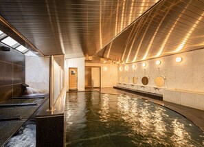 Una piscina interior moderna con superficie de agua cristalina, una puerta de madera y varios espejos circulares en la pared.