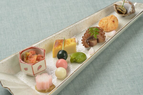 Un plato de cerámica rectangular con distintos alimentos, como un trozo de queso, un pulpo y varios elementos pequeños y redondos de colores.