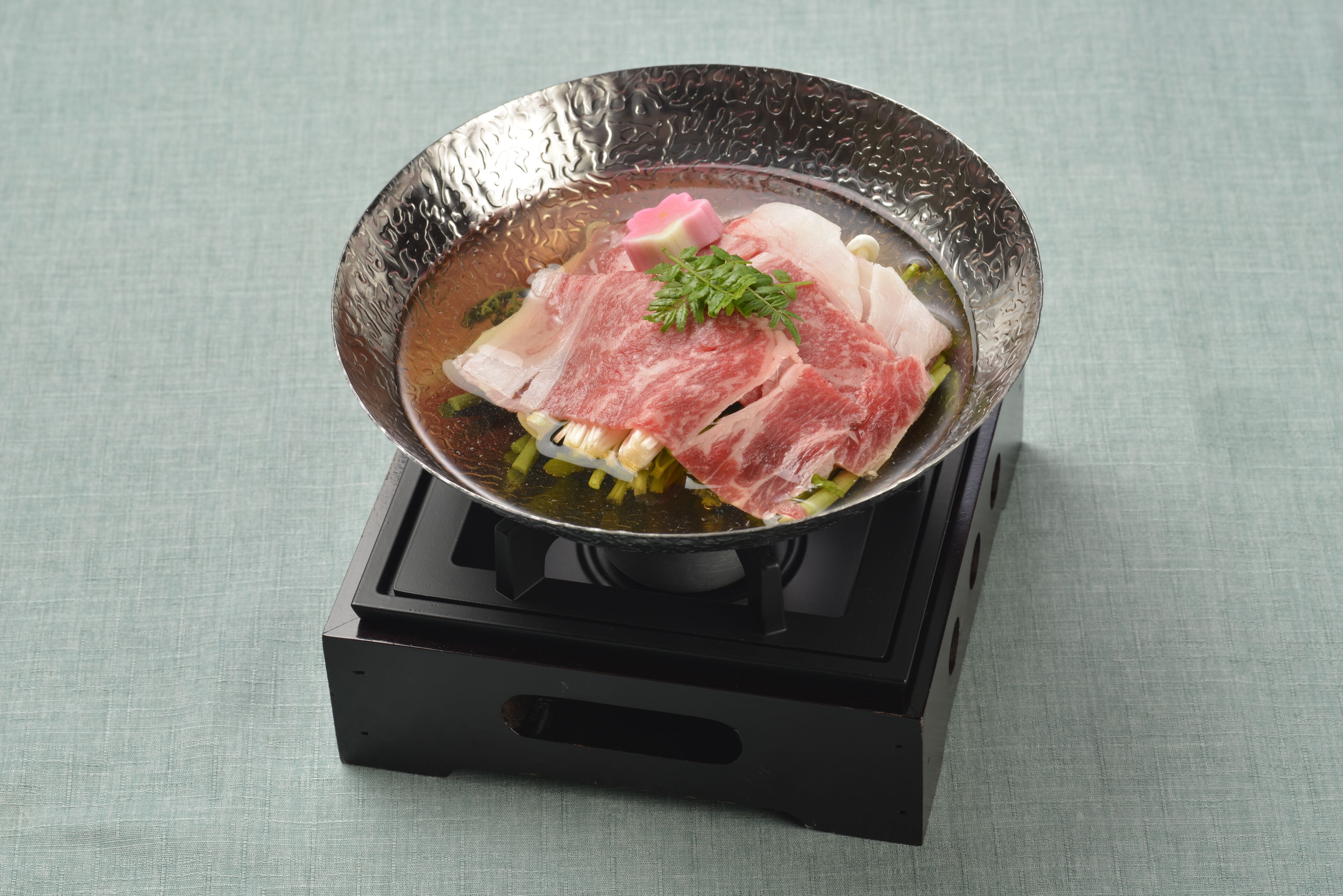 A pot on a stove with raw meat and vegetables.