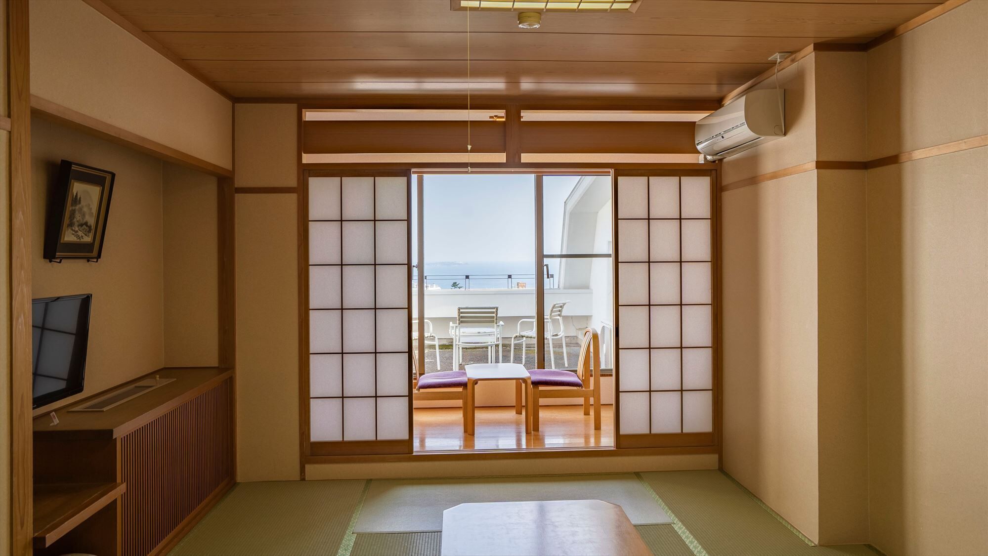 Una tradizionale stanza giapponese con pavimento in tatami, un paravento scorrevole shoji, un televisore e vista sul mare.