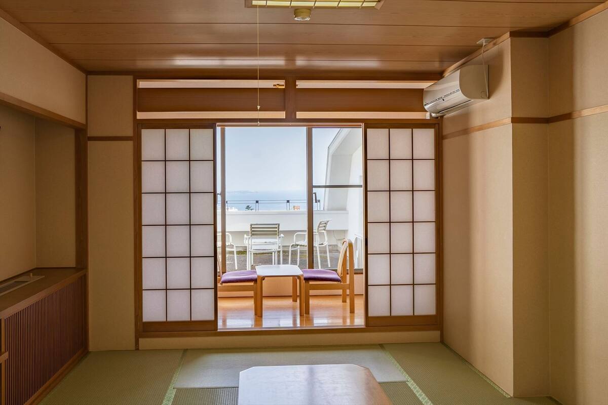 Una tradizionale stanza giapponese con pavimento in tatami, un paravento scorrevole shoji, un televisore e vista sul mare.